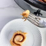 Piece of cinnamon roll on a fork over a white plate with cinnamon roll on it.