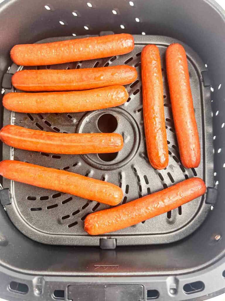 Fully cooked hot dogs in an air fryer basket.