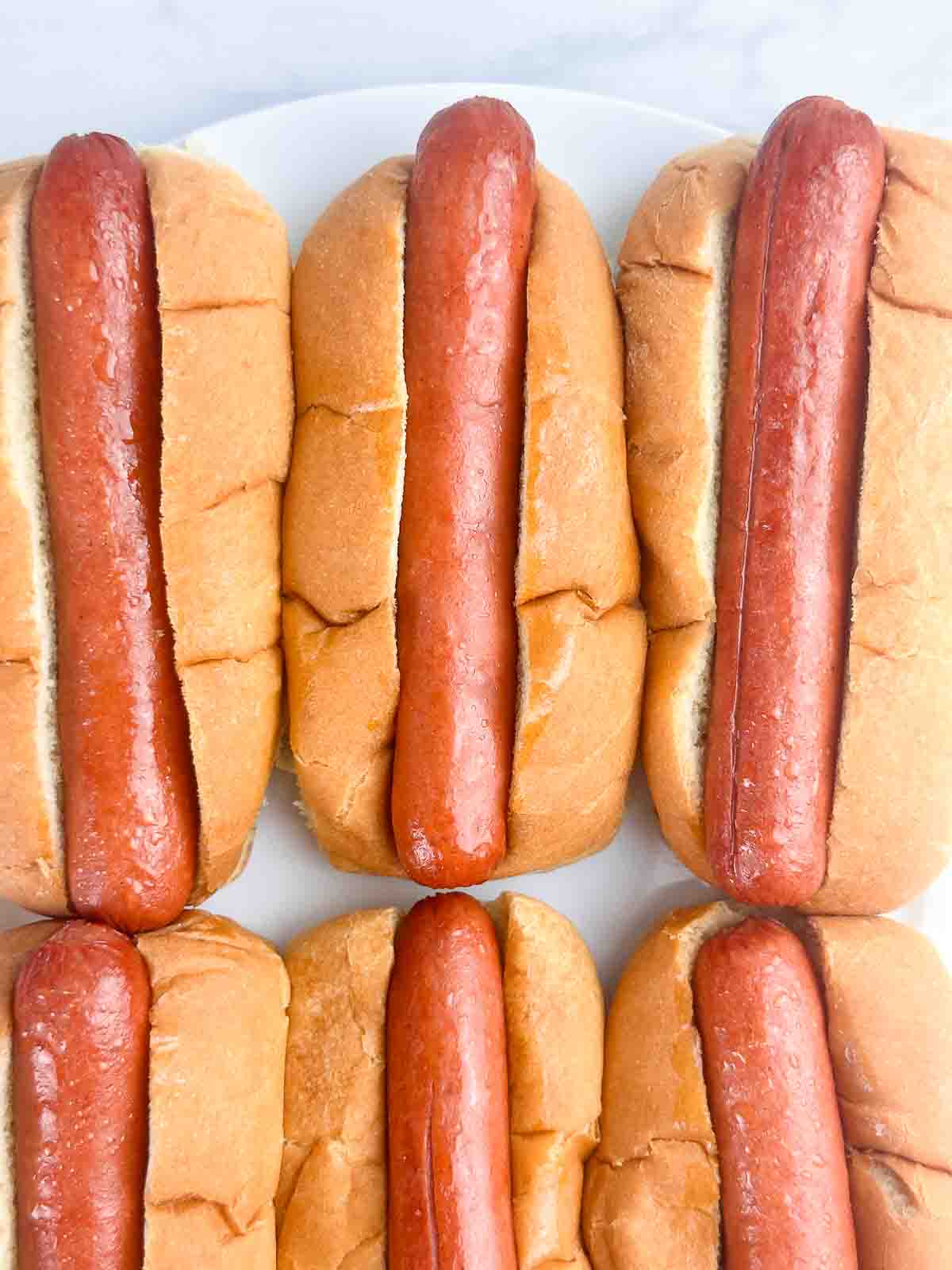 Air fryer hot dogs in buns on a white plate.