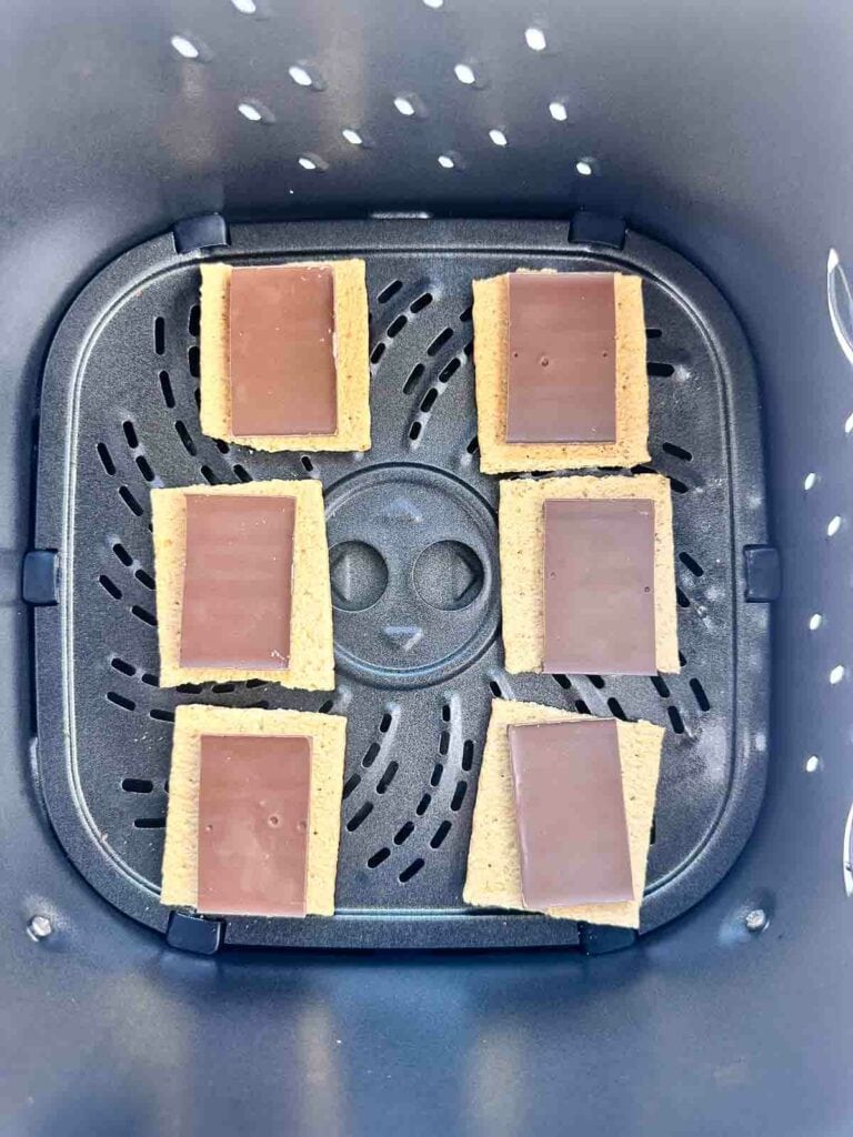 Chocolate bar on top of graham cracker squares in air fryer basket.