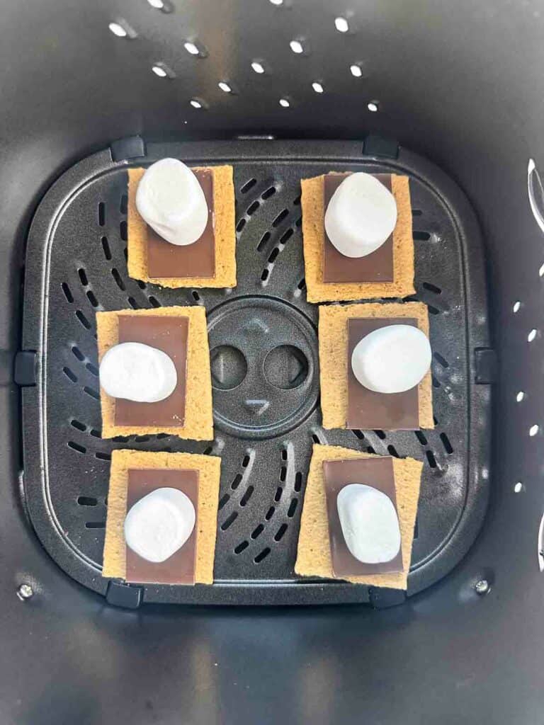 Marshmallows on top of chocolate and graham crackers in an air fryer basket.