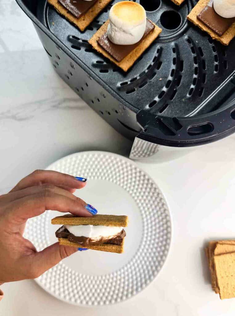 Air fryer smore ready to eat, held above a white plate.