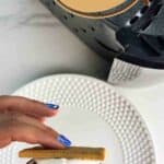 Hand holding an air fryer smore over a white plate, text reads air fryer smores, whatacrockof.com