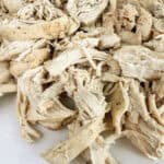 Shredded chicken on a white cutting board.