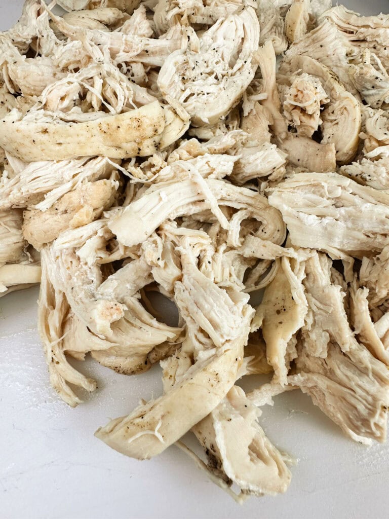 Shredded chicken on a white cutting board.